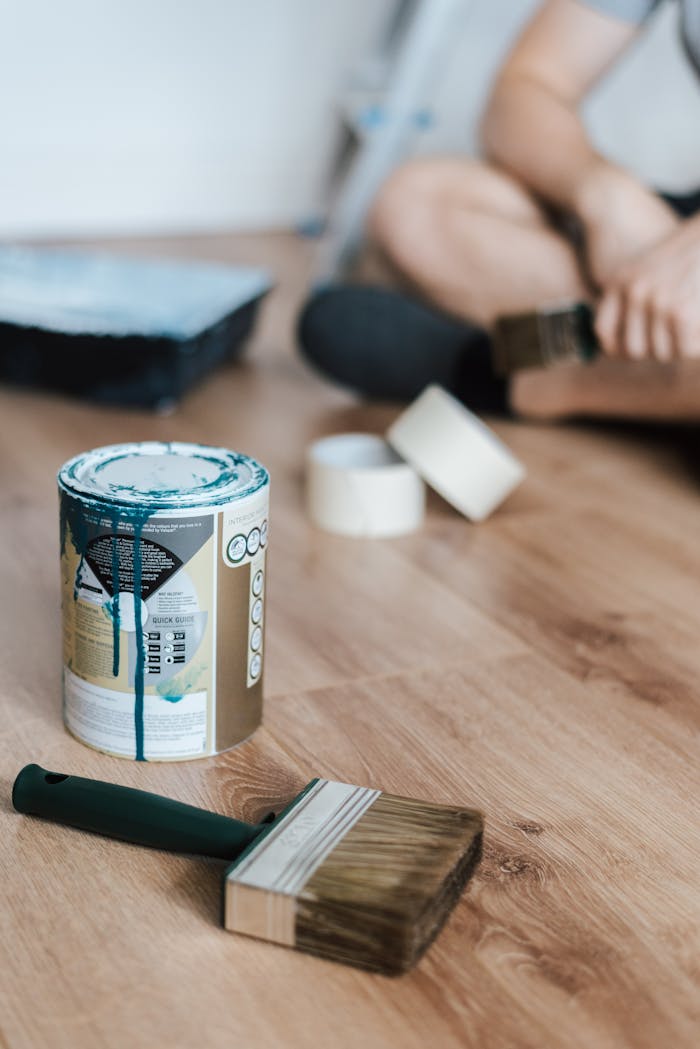 Crop anonymous male sitting with crossed legs on parquet near professional paint brush in house during renovation process
